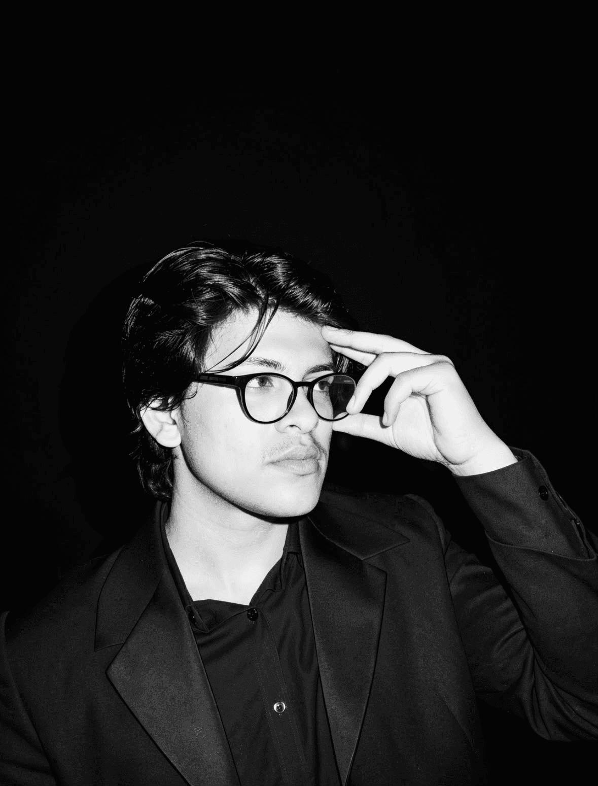 Shivansh Srivastava in a black suit and glasses, looking into camera